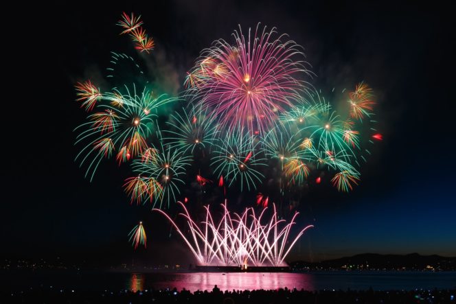 fireworks or red, green and yellow explode above vancouver's Enlgish bay and reflect upon the sea below.
